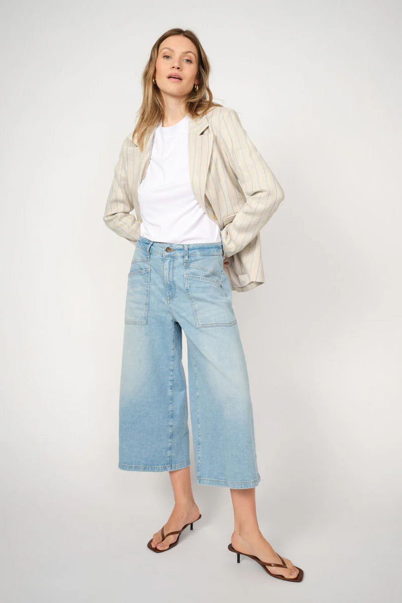 Woman wearing a beige jacket, white shirt, and light blue jeans on a white background