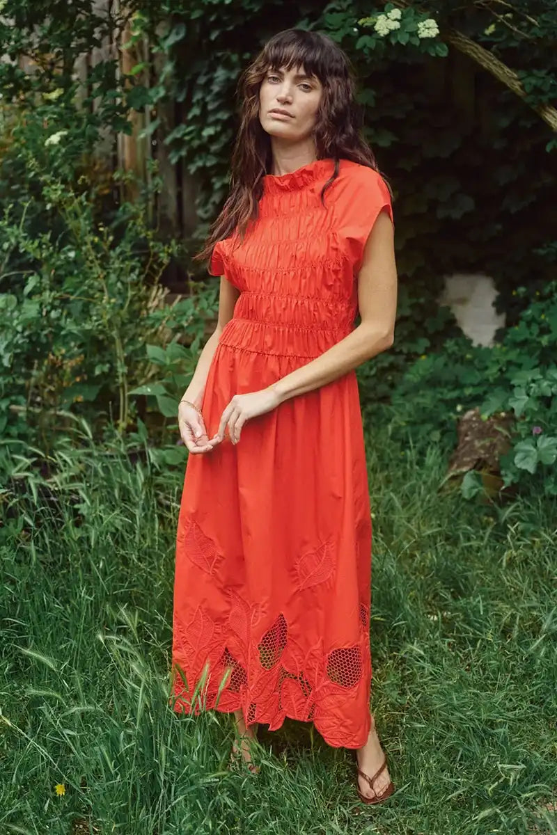 Woman in a red dress standing in a grassy area with greenery