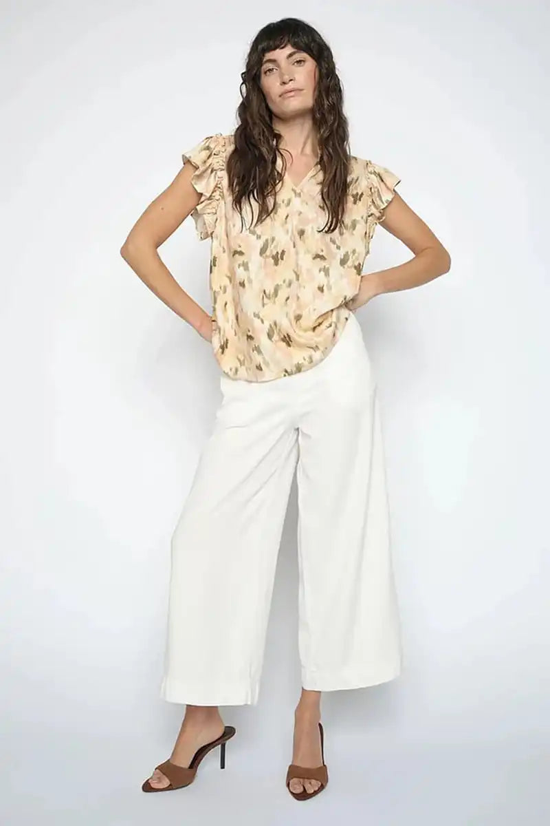 Woman wearing a floral blouse and white pants on a plain background