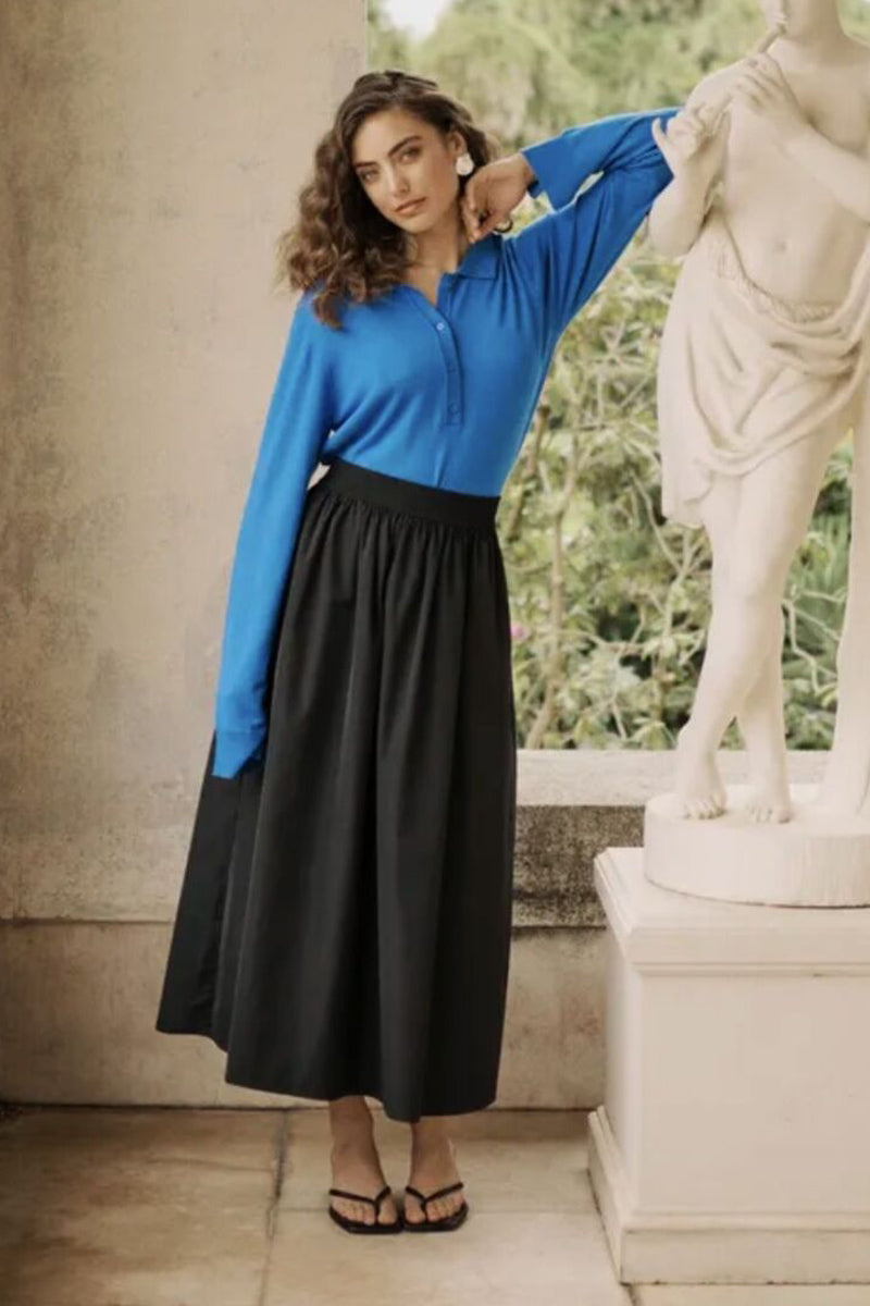 Woman in a blue top and black skirt standing next to a statue outdoors.