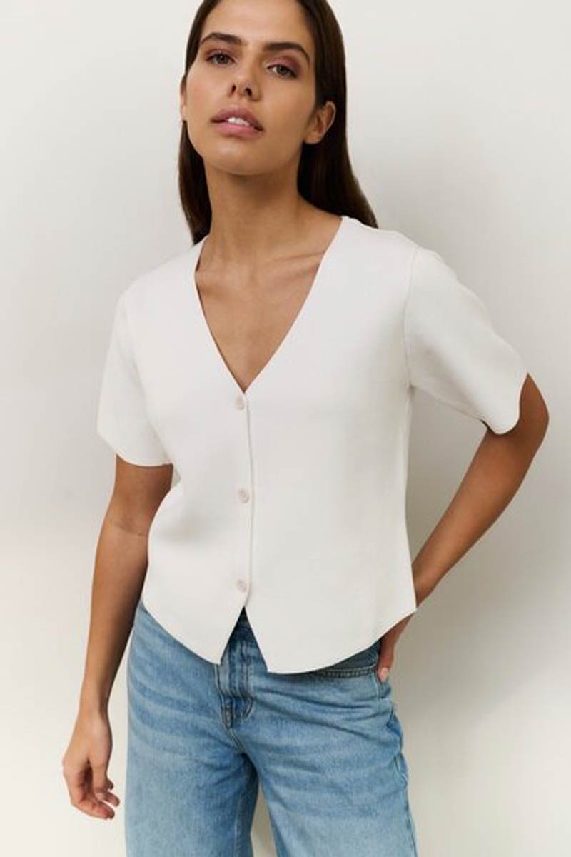 Woman wearing a white blouse and blue jeans against a plain background